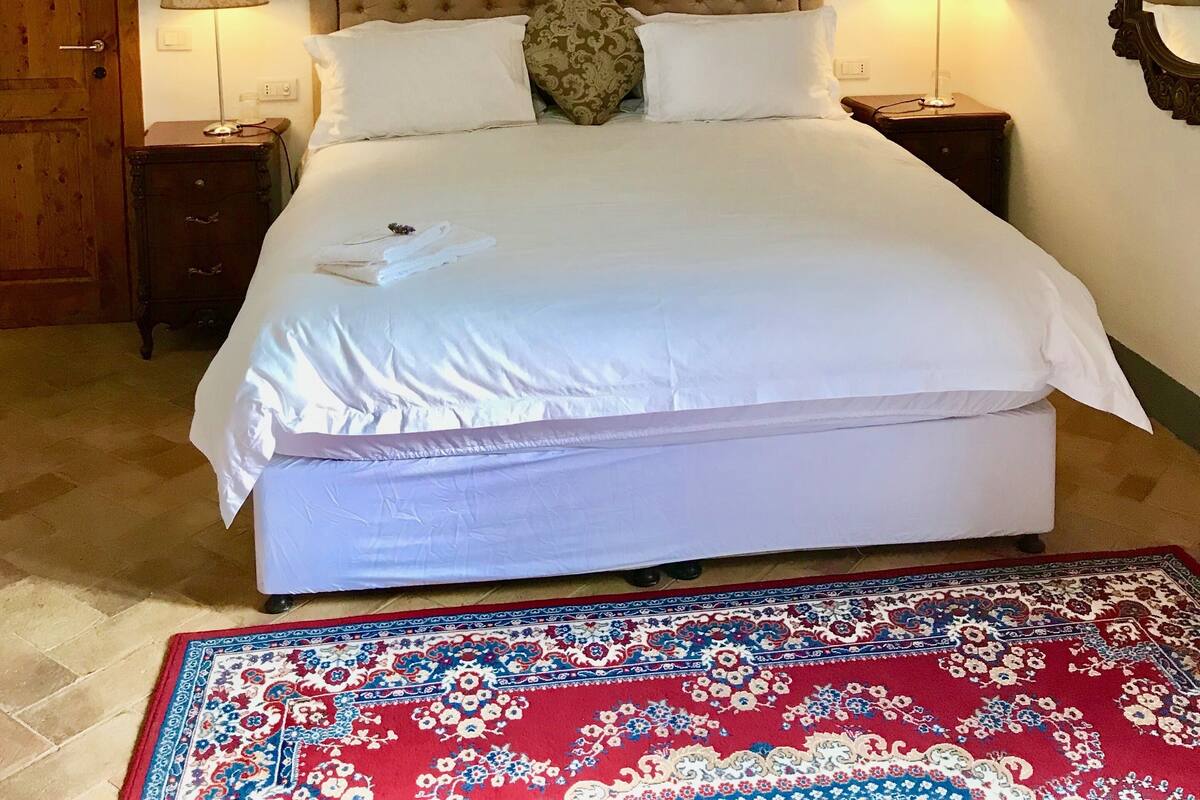 Ein Schlafzimmer mit einem großen Bett, zwei Nachttischlampen, einer Holzbalkendecke, einer Holztür und einem roten Teppich mit Muster.