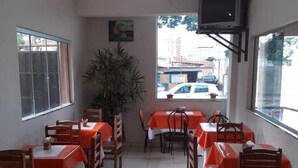 En restaurant med borde dækket af orange dug, træstole, en loftsvifte og et fjernsyn monteret på væggen.