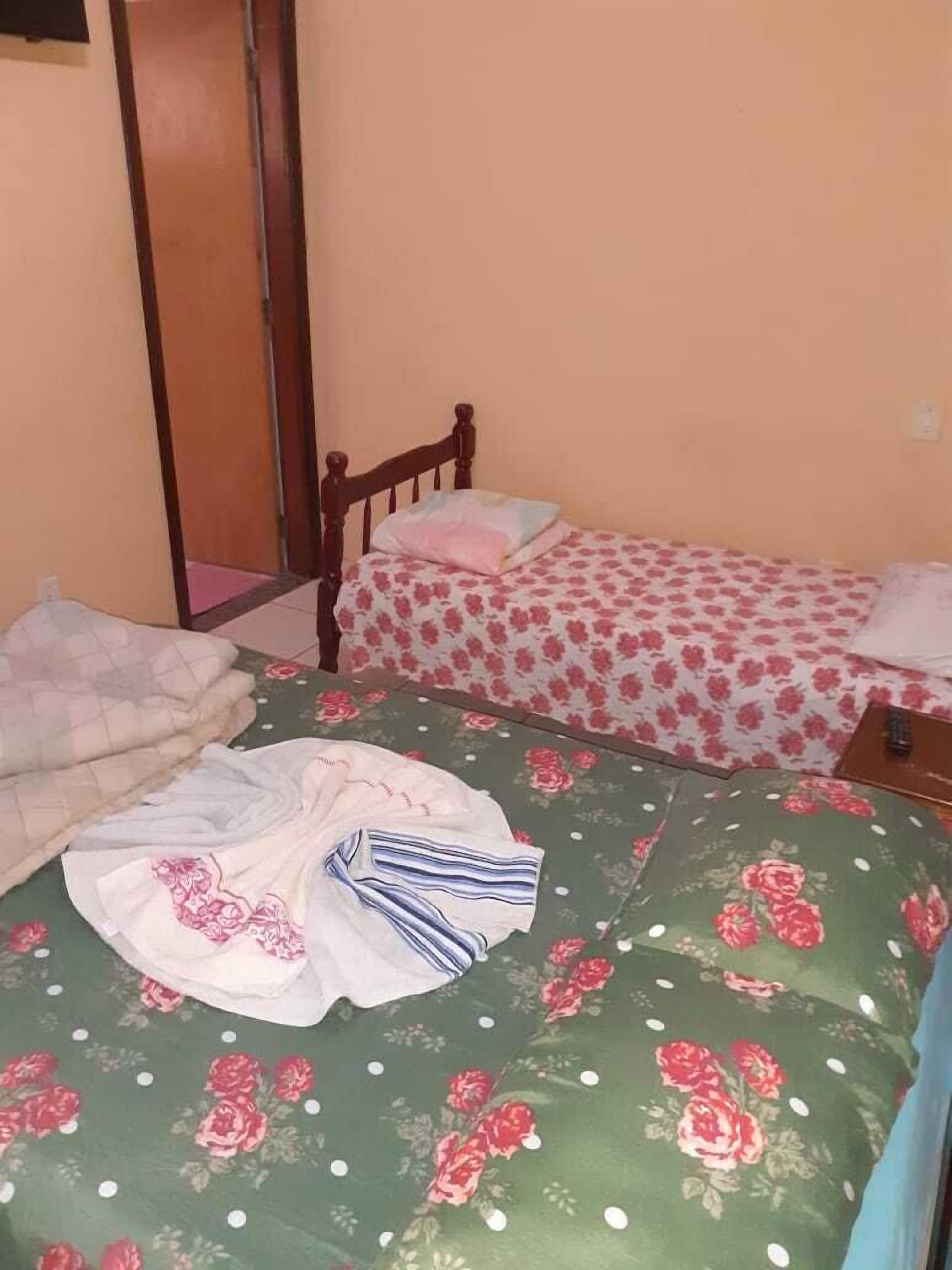 A small, single-room bedroom with two beds, one with a floral bedspread and the other with a striped bedspread.