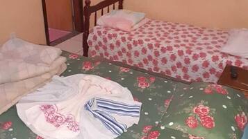 A small, single-room bedroom with two beds, one with a floral bedspread and the other with a striped bedspread.