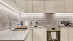Eine moderne Küche mit weißen Schränken, einer Edelstahl-Spüle, einem Wasserkocher, einer Mikrowelle und einem eingebauten Backofen.