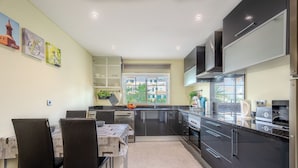 A modern kitchen with black cabinets, a dining area with a table and chairs, and a window with a view of buildings.