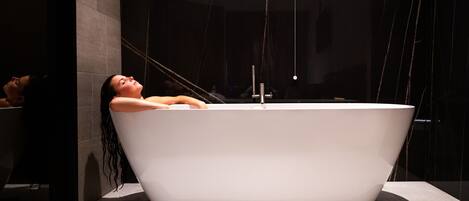 Une salle de bain moderne avec une baignoire sur pieds, un grand miroir et un mur de couleur sombre.