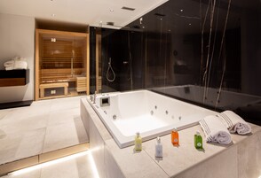 A modern bathroom with a large bathtub, a wooden bench, and a glass shower enclosure.