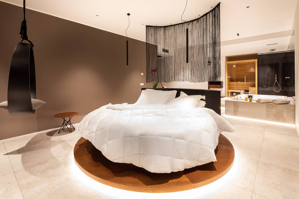 A modern bedroom with a circular wooden bed, a hanging chair, and a wooden wardrobe.