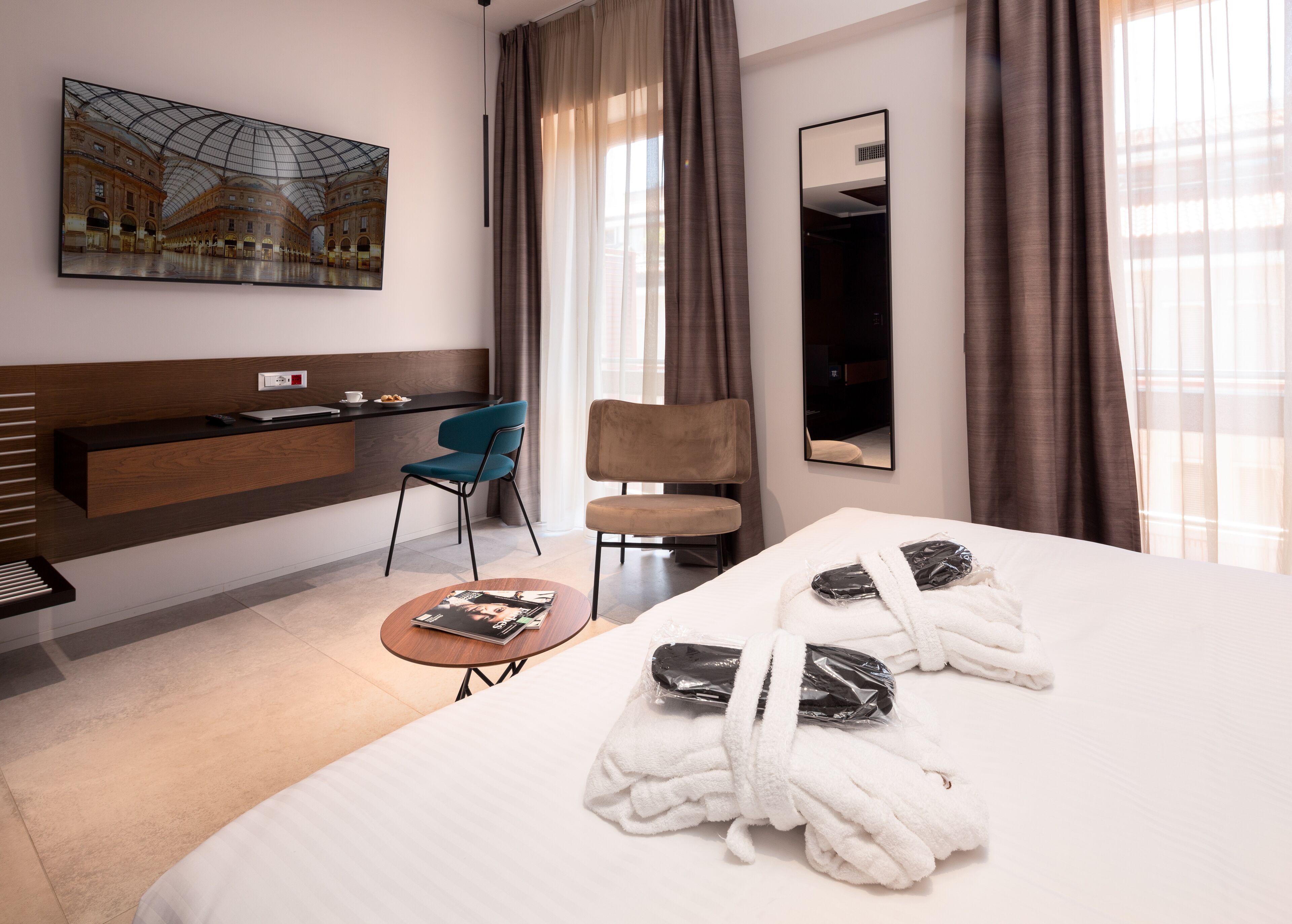 Una habitación de hotel con una cama grande, un escritorio con computadora, una silla, una mesa de centro y un cuadro de una estación de tren en la pared.