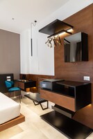 Una moderna camera d'albergo con un letto, una scrivania con un portatile, una sedia, uno specchio e un lampadario originale.