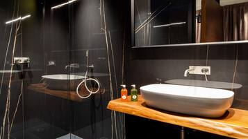 Un baño moderno con ducha de vidrio, tocador de madera con un lavamanos grande y un espejo sobre el tocador.
