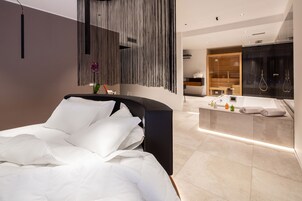 A modern bedroom with a large bed, a bedside table, and a bathroom with a vanity and shower.