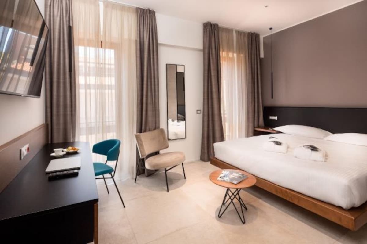 A modern hotel room with a bed, a desk, a chair, a small table, and a TV.
