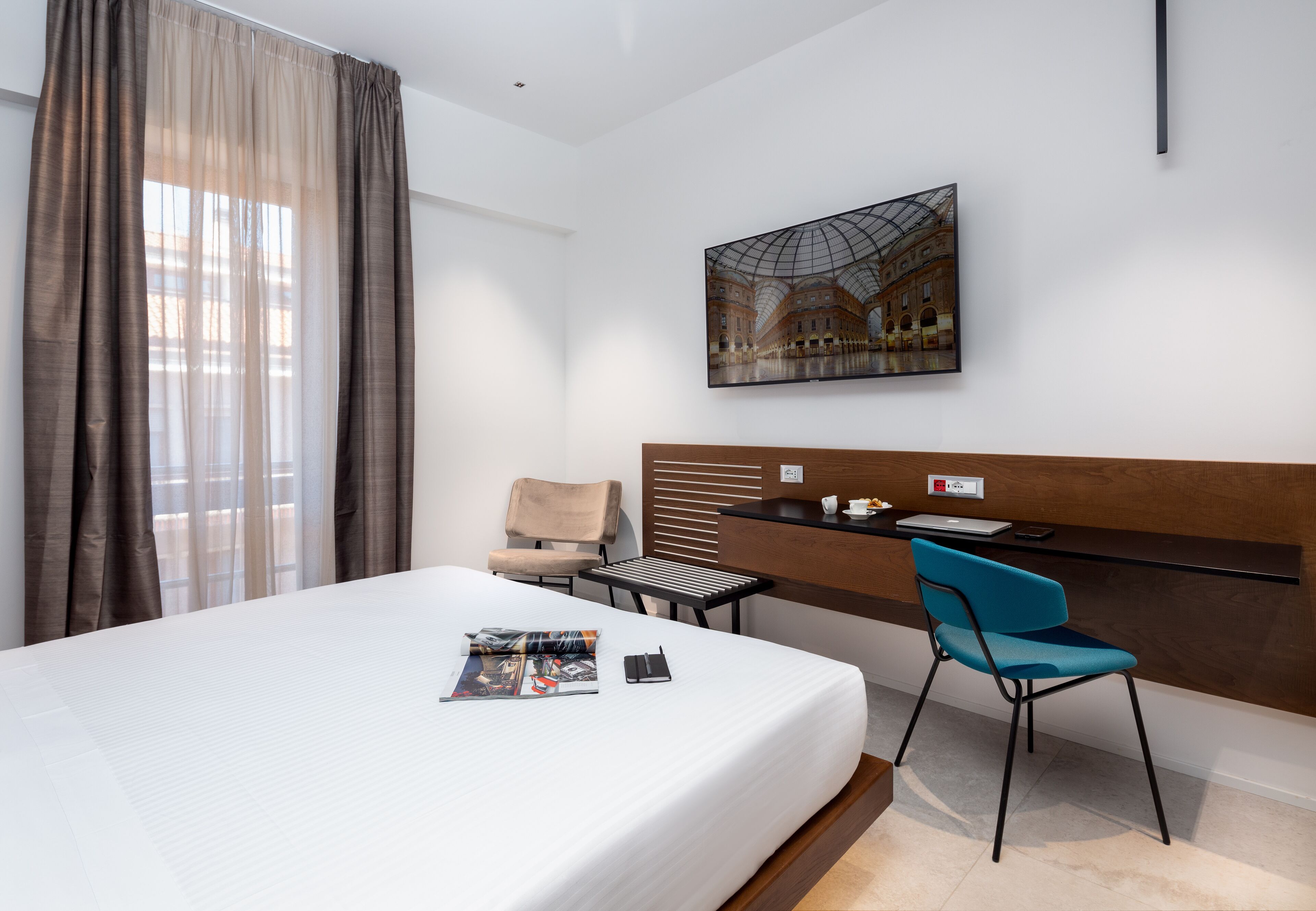 A hotel room with a large bed, a desk with a chair, a painting on the wall, and a window with curtains.