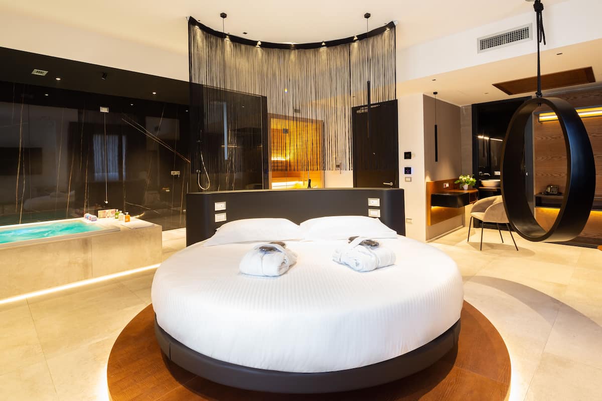 A modern hotel room with a circular bed, a large window, a jacuzzi, and a hanging chair.