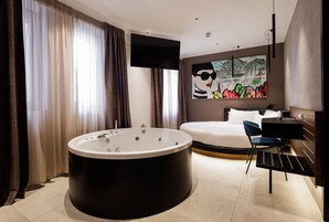 Een moderne hotelkamer met een groot bad, een bed, een bureau en een schilderij aan de muur.
