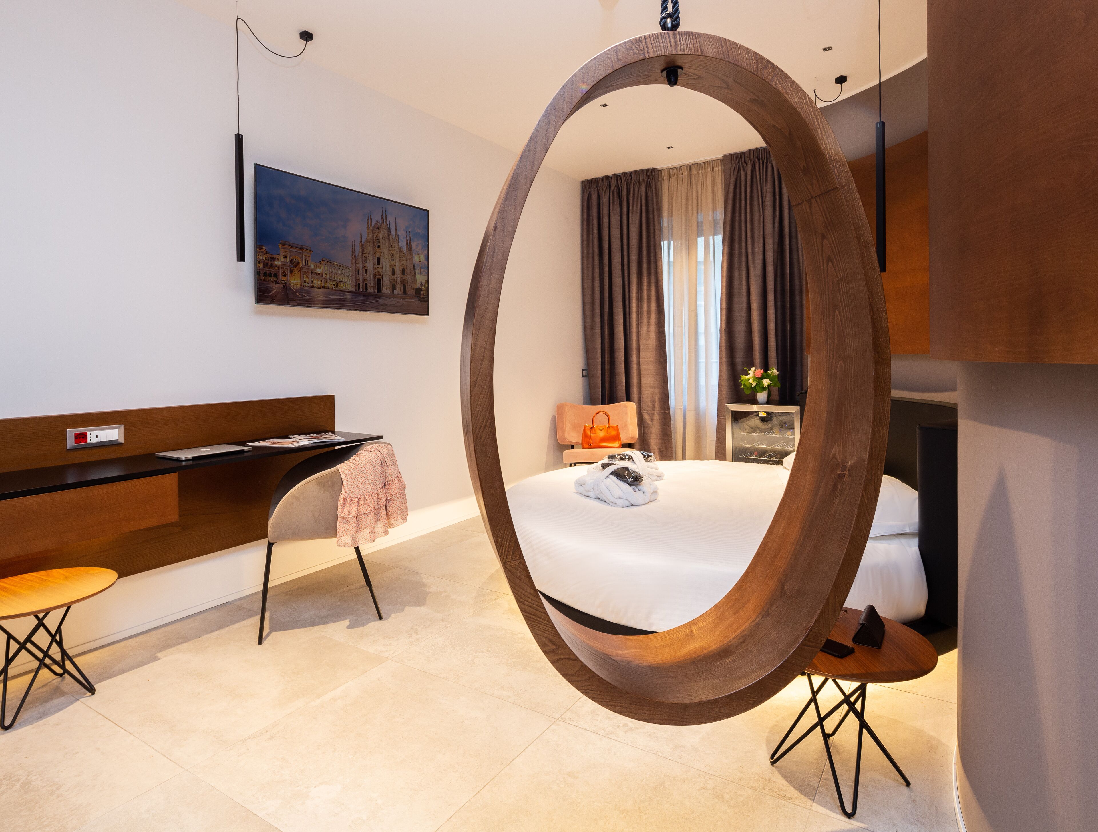 A modern hotel room with a large bed, a desk, a chair, and a circular mirror.