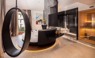 Una camera d'albergo moderna con una reception nera a forma di curva, una sedia sospesa, un'ampia finestra con vista sulla città e un quadro appeso al muro.