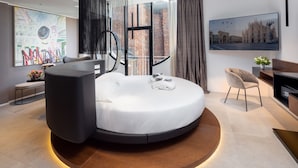 A modern bedroom with a circular bed, a large window with a city view, and a large artwork on the wall. - The Corner Duomo Hotel (Milan)