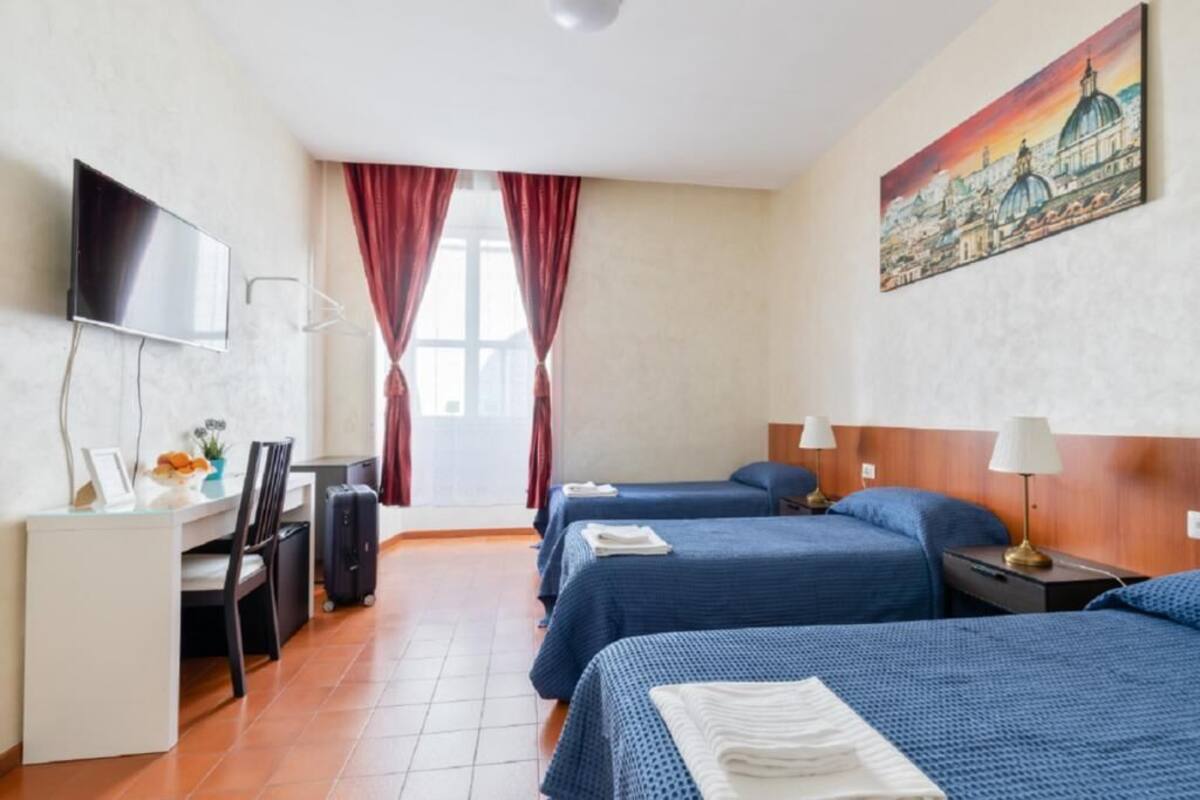 A hotel room with two beds, a desk with a chair, a TV, and a painting on the wall.