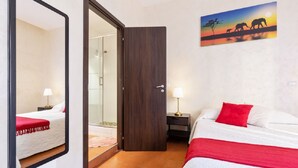A hotel room with a bed, a nightstand, a mirror, a door, and a painting of elephants on a sunset. - Roma Enrico Guesthouse (Rome)