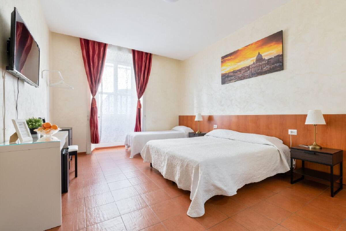 A hotel room with two beds, a desk with a computer, a TV, and a painting of a sunset.