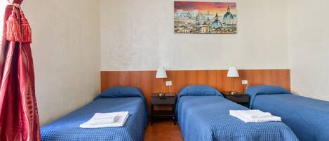 A hotel room with two beds, each with a blue bedspread and white towels, a wooden headboard, a painting of a cityscape on the wall, and a red curtain on the left.