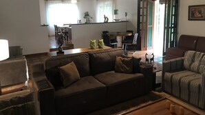 Un salon avec un canapé, un divan à rayures, une table à manger avec des chaises, et un coin cuisine à l’arrière-plan.