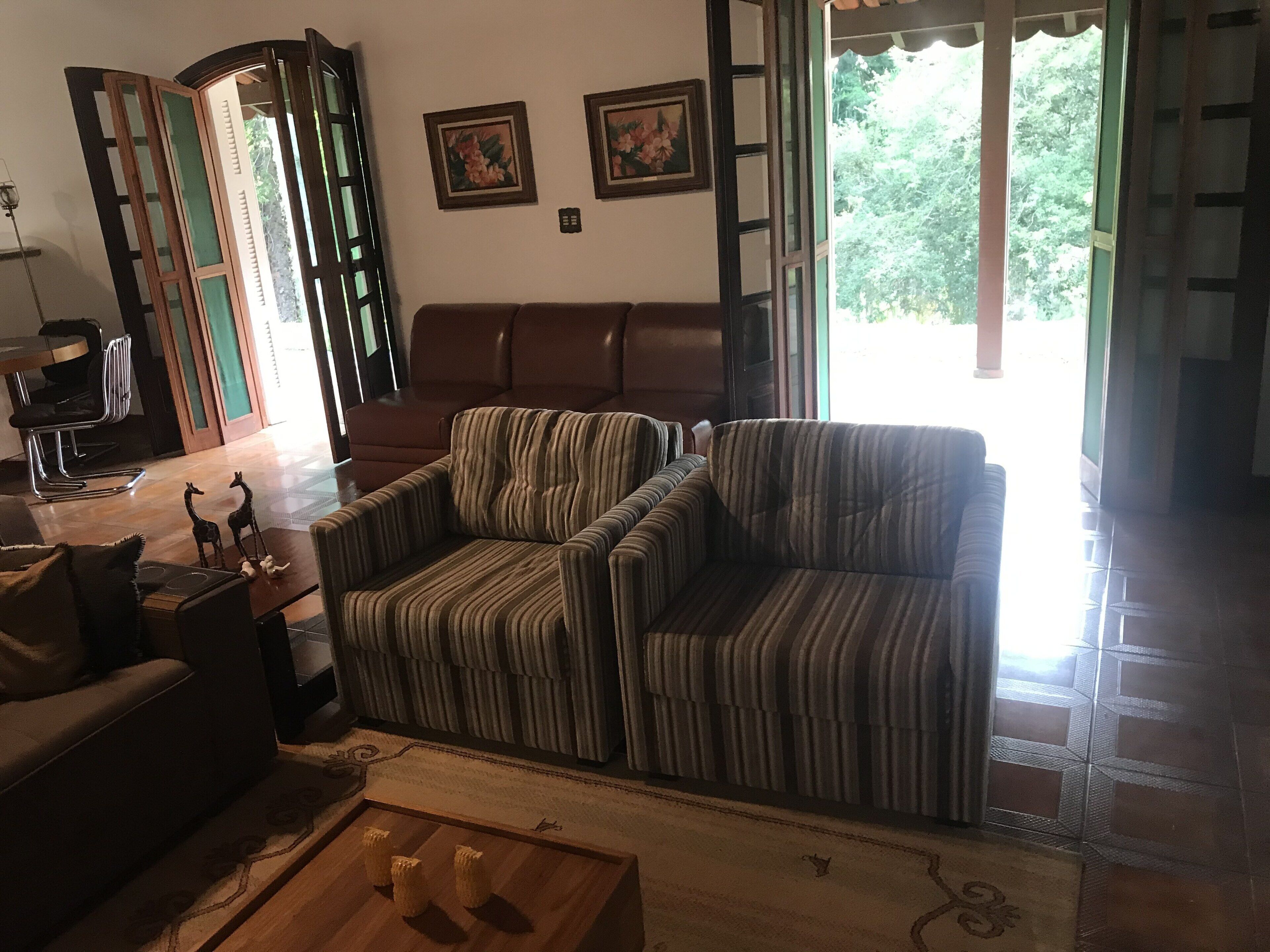 A living room with a striped sofa, a wooden coffee table with decorative items, a brown armchair, and a dining area with a chair and table.