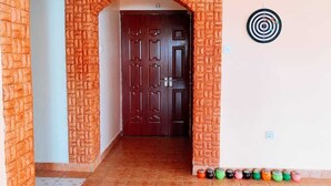 A hallway with a brick archway leading to a dark wooden door. There is a dartboard on the wall to the right. - NAIROBI SIMBA YOUTH HOSTELS (Syokimau)