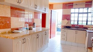 A kitchen with white cabinets, a marble countertop, and a window. - NAIROBI SIMBA YOUTH HOSTELS (Syokimau)