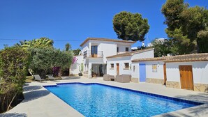 Une maison à deux étages avec une piscine, entourée de verdure et d’arbres.