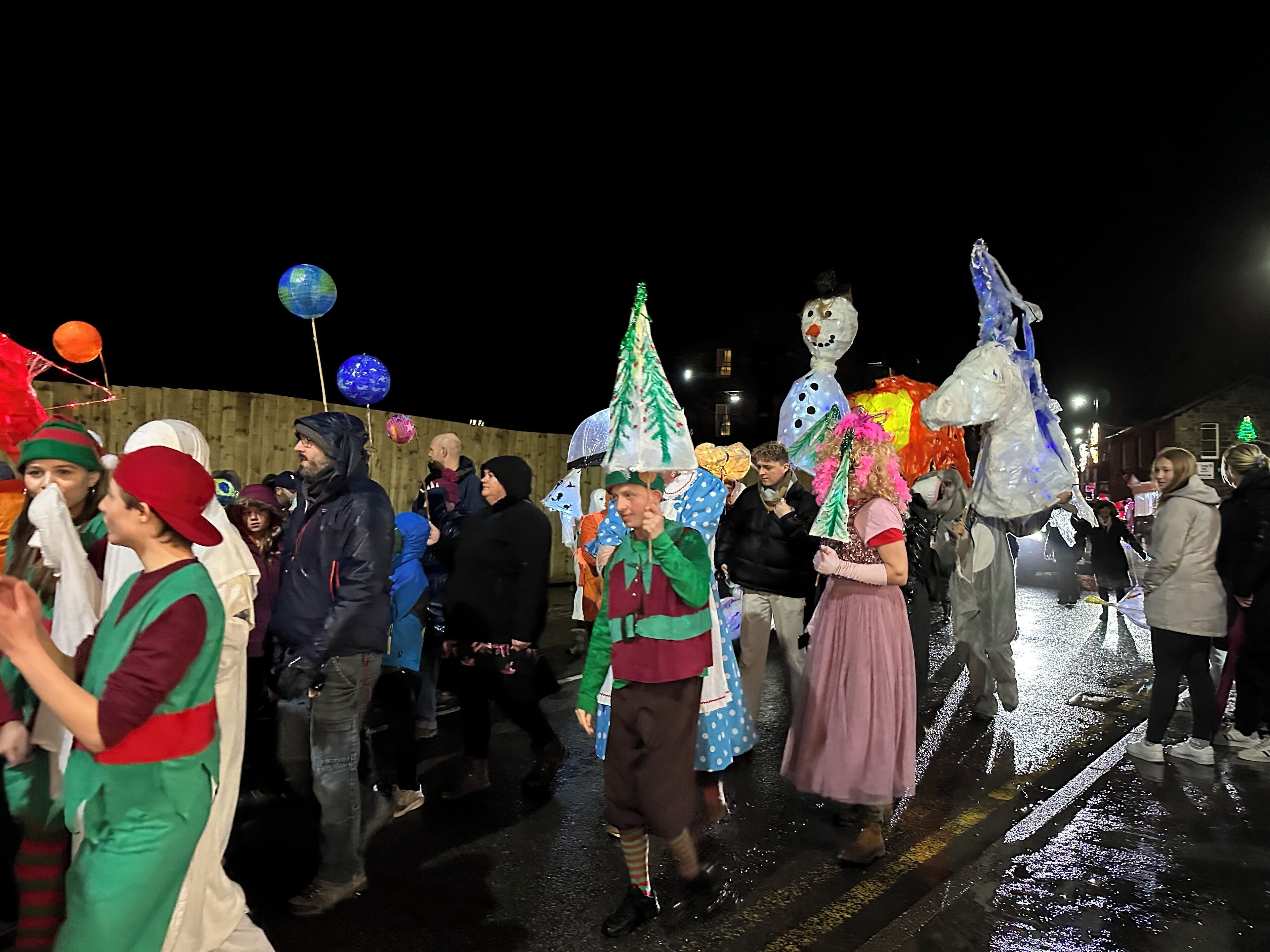 A group of people in festive costumes walking on a wet street at night.