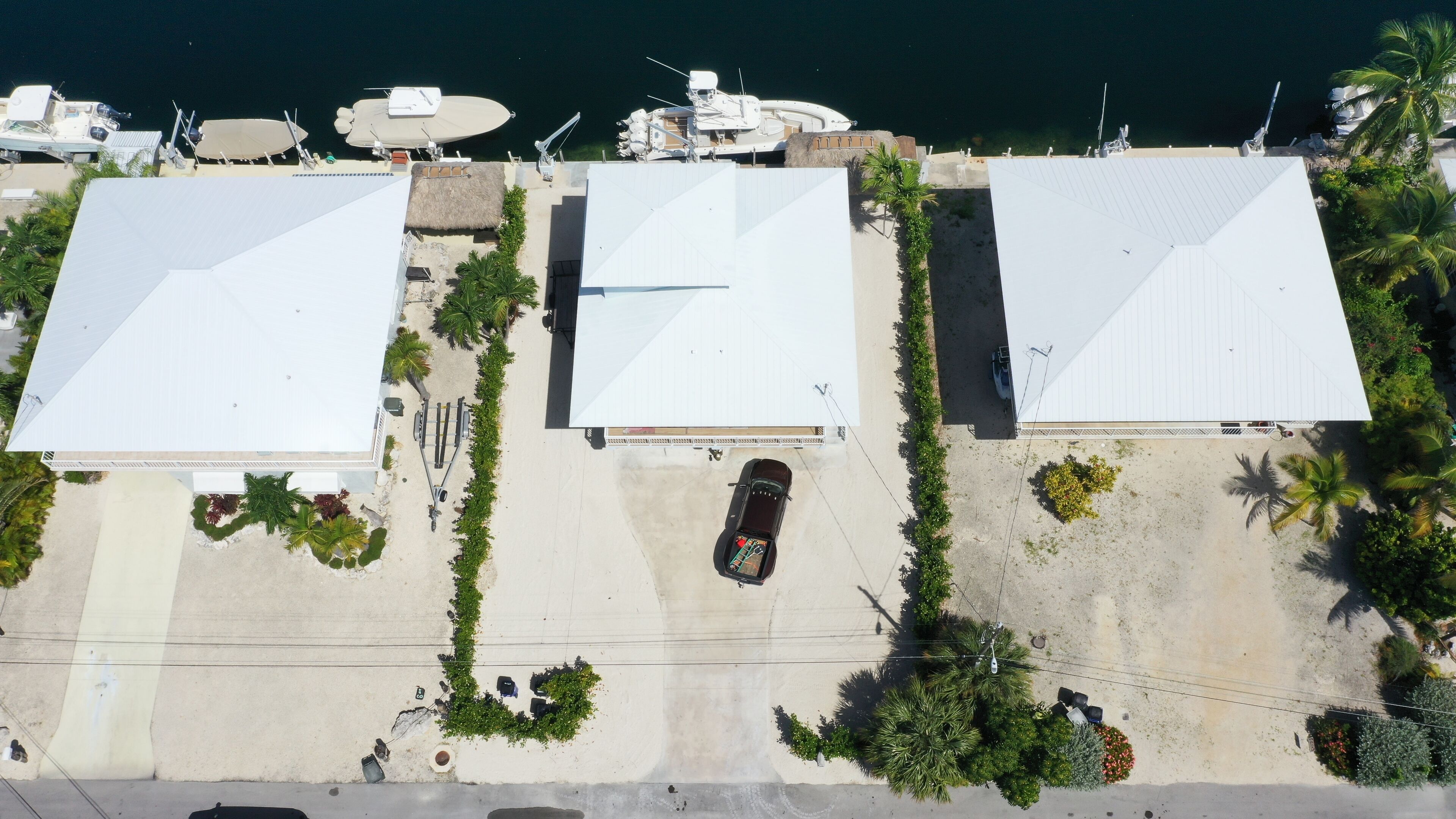 An aerial view of a coastal property with three large buildings, a paved driveway, and a parked car.