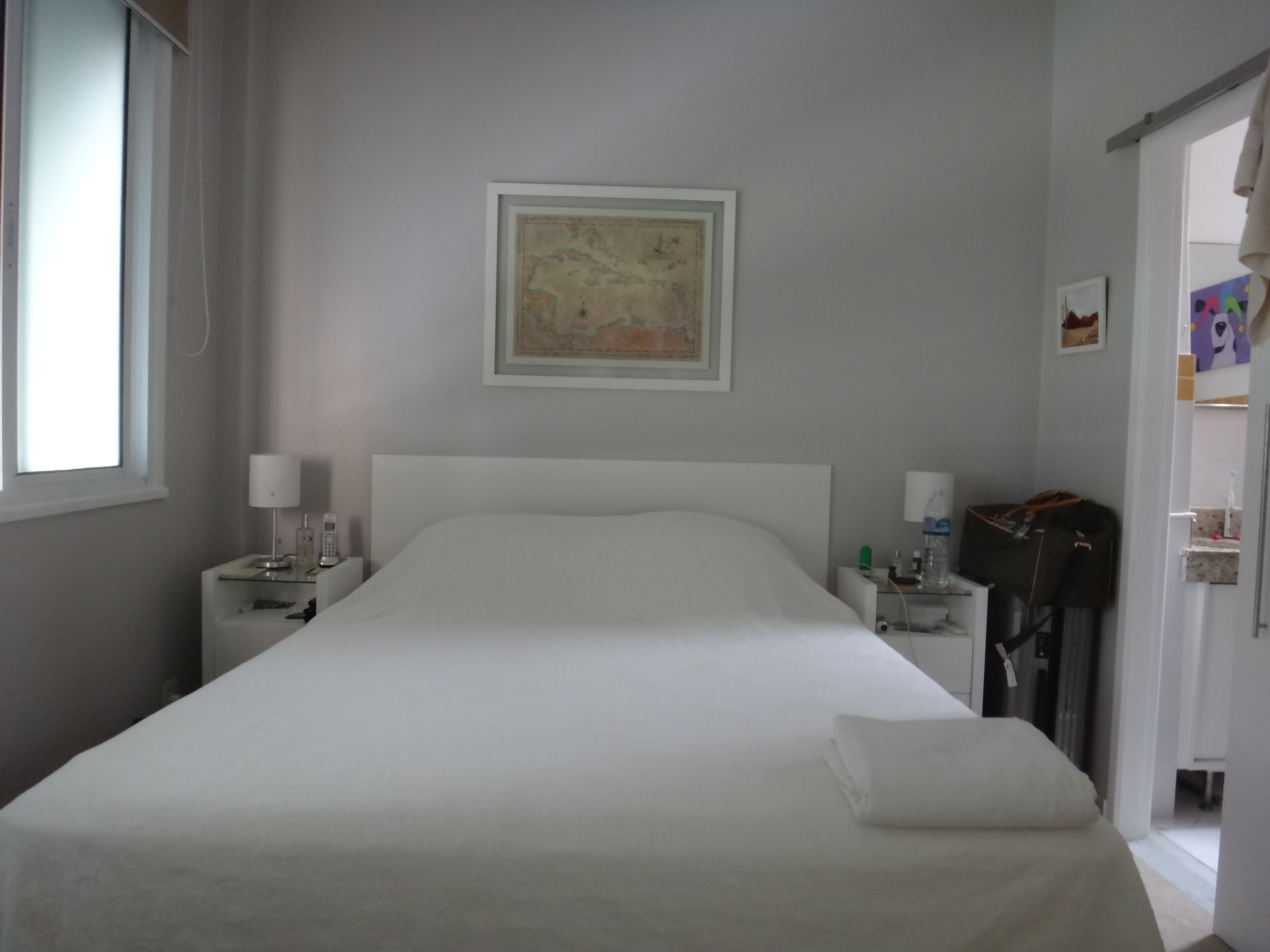 A hotel room with a bed, a nightstand, a lamp, a framed map on the wall, and a suitcase on the floor.