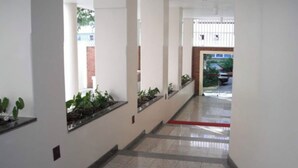 A corridor with white walls, tiled flooring, and potted plants along the walls.