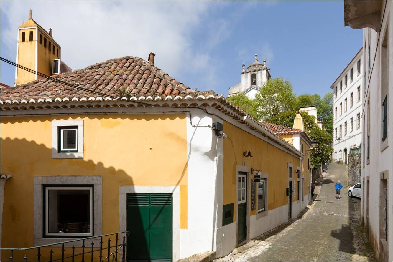 A narrow street with yellow buildings, a bell tower, and a church in the background.