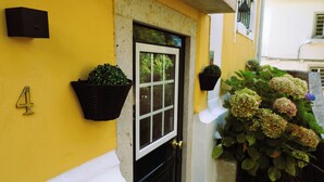 A yellow building with a black door and window, a mailbox, and hanging flower baskets.