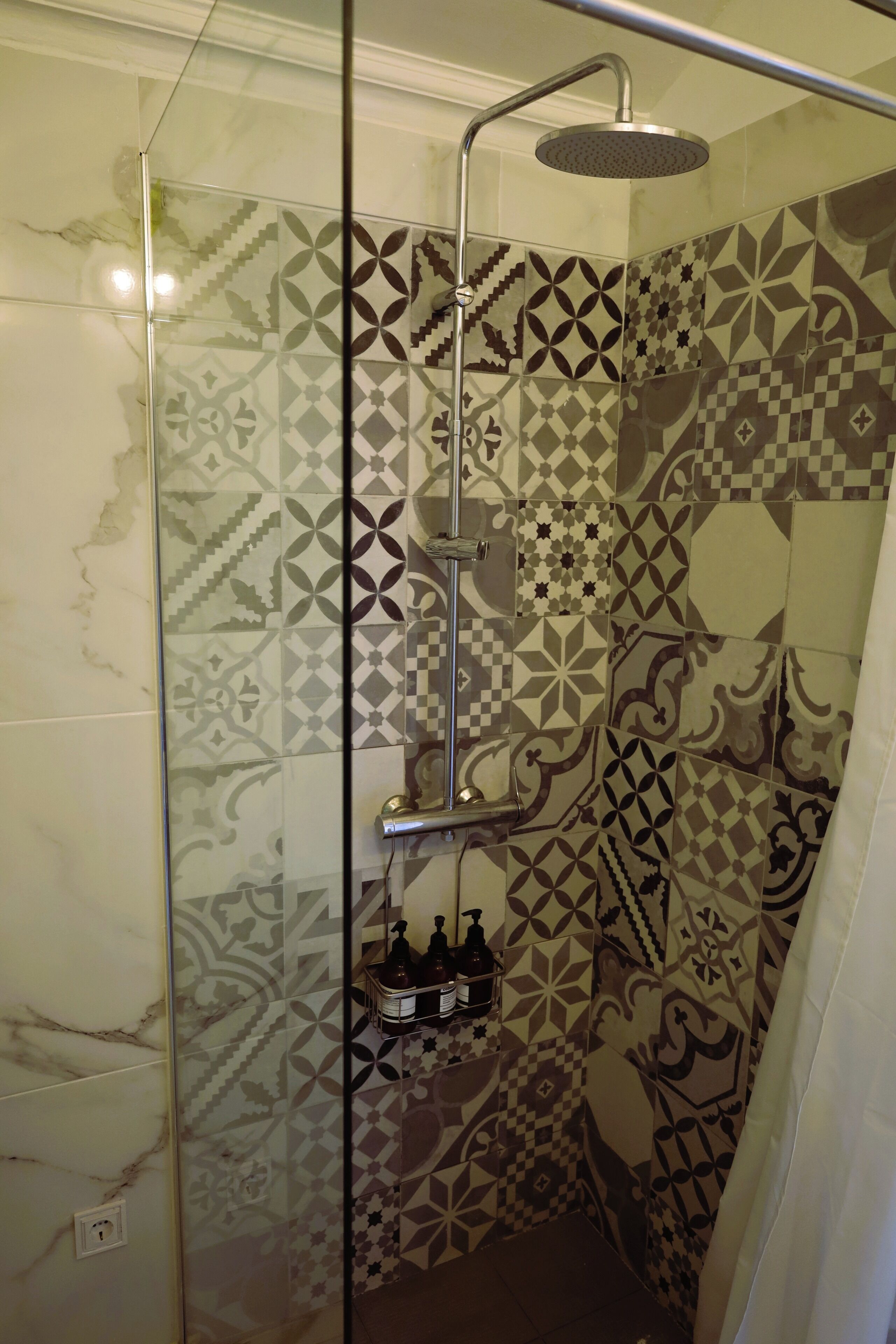 A shower with a glass door, a handheld showerhead, and a wall with patterned tiles.