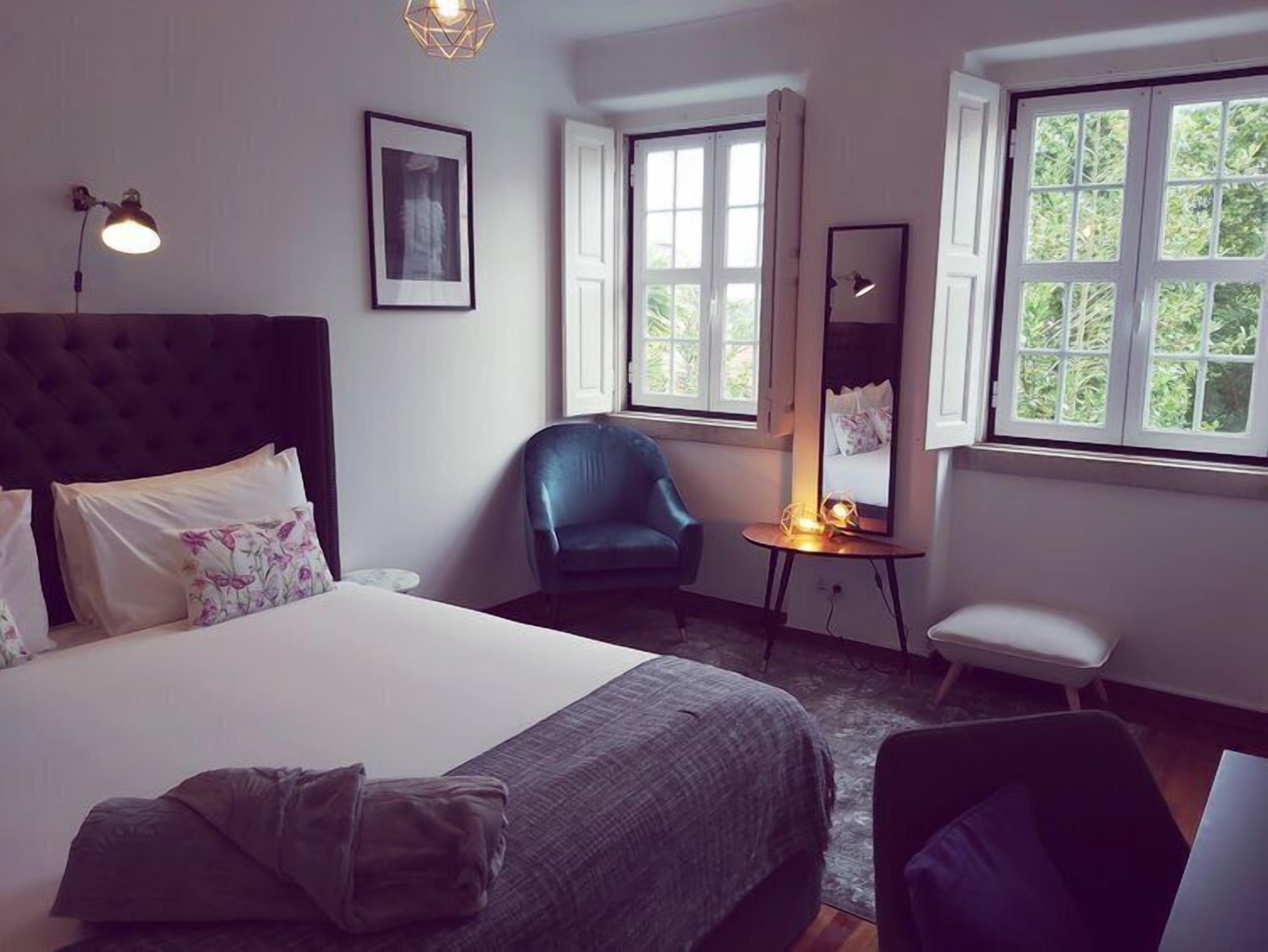 A hotel room with a large bed, a chair, a desk, and a window with a view of greenery.