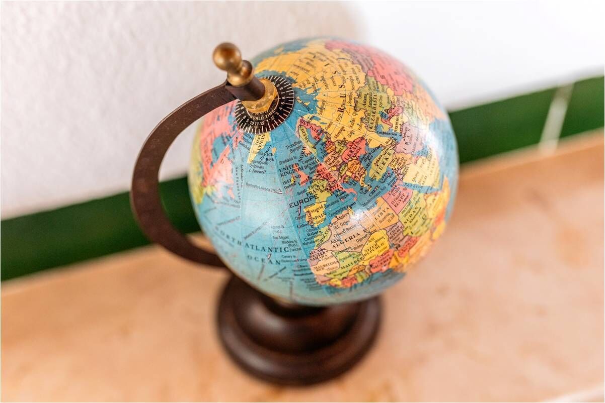Un globe posé sur un support en bois, doté d’un bouton en laiton, le tout placé sur une surface dont le fond est vert et blanc.