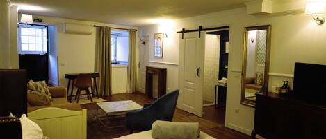 A hotel room with a bed, a desk, a chair, a sofa, a TV, and a bathroom visible through an open door.