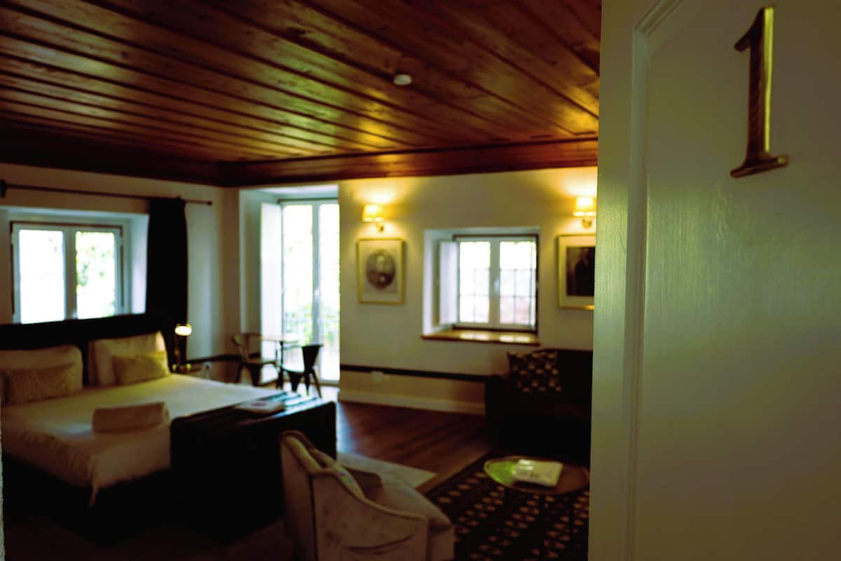 A room with a wooden ceiling, a bed, a chair, and a desk.