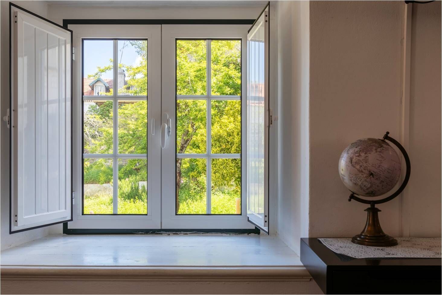 A room with a large window, a globe on a table, and a view of greenery outside.