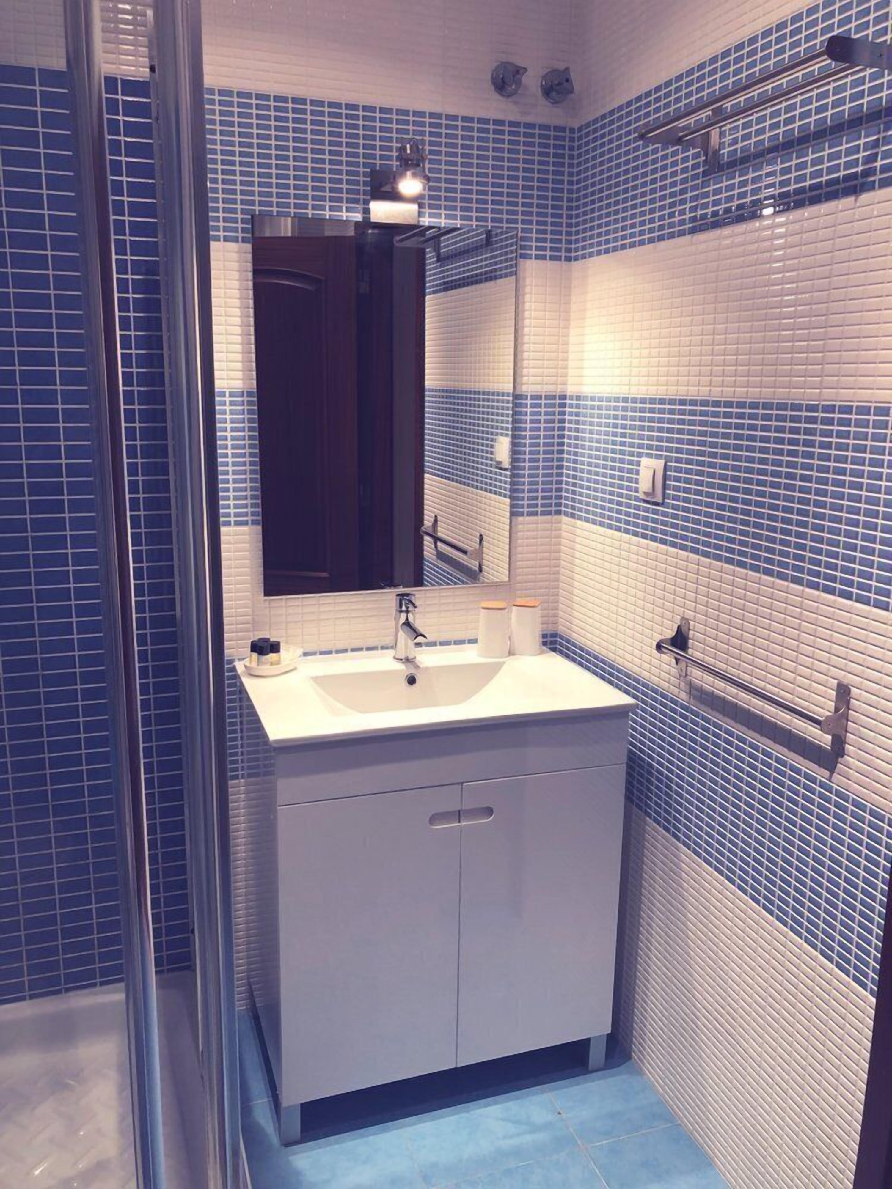 Un baño con un lavamanos blanco, un espejo y paredes con azulejos azules.
