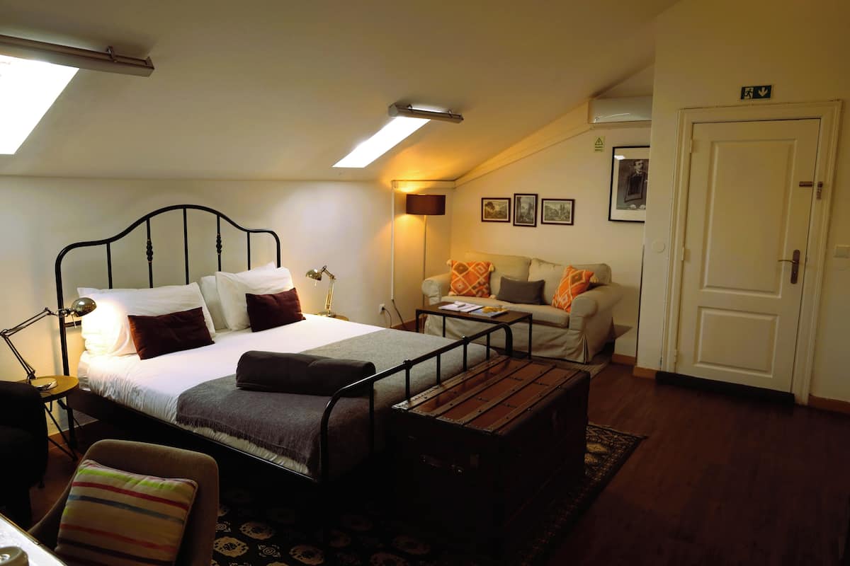 A bedroom with a bed, bedside table, lamp, and a sofa.