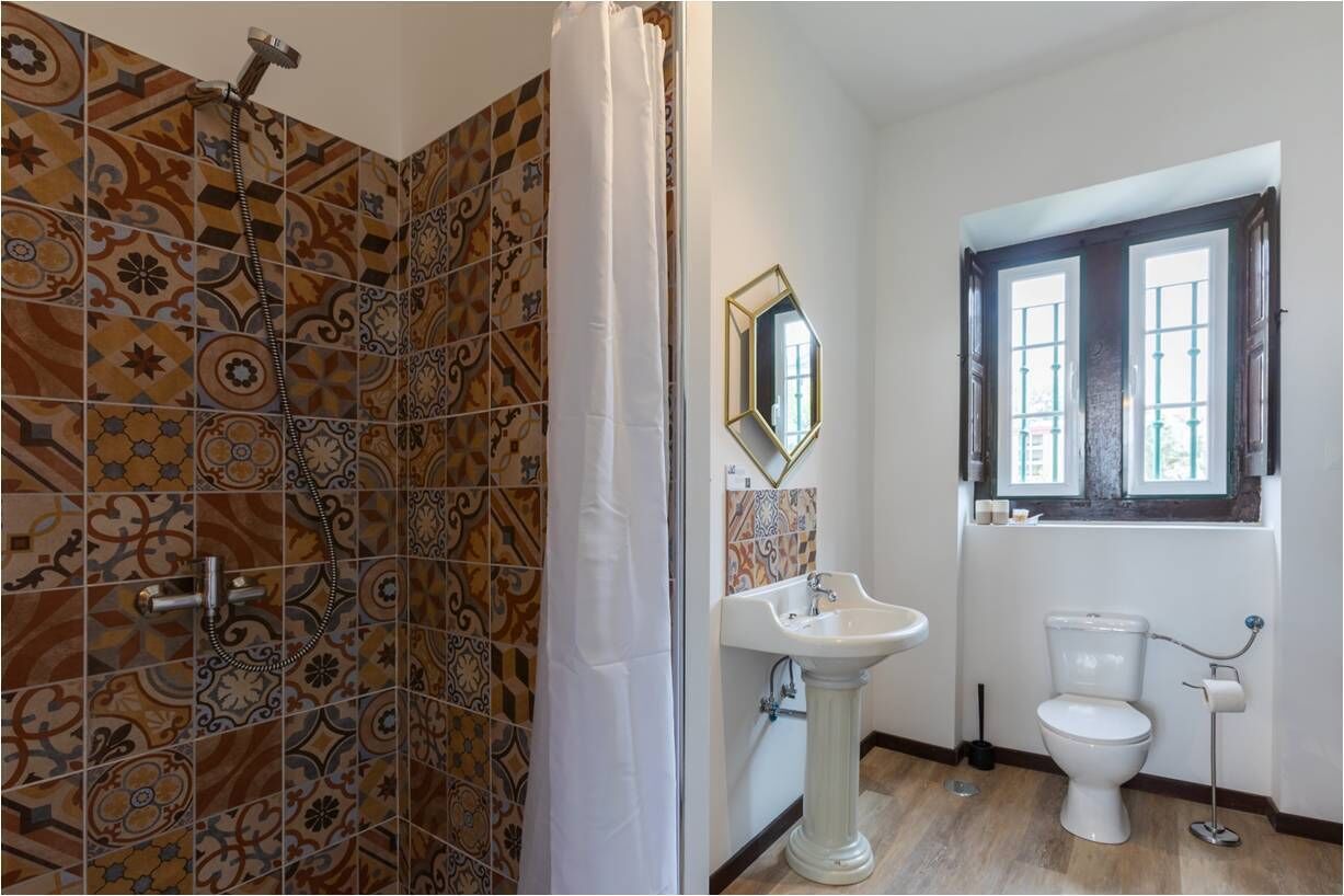 Une salle de bain avec des carreaux décorés, un lavabo sur pied, des toilettes et une fenêtre donnant sur un beau paysage.