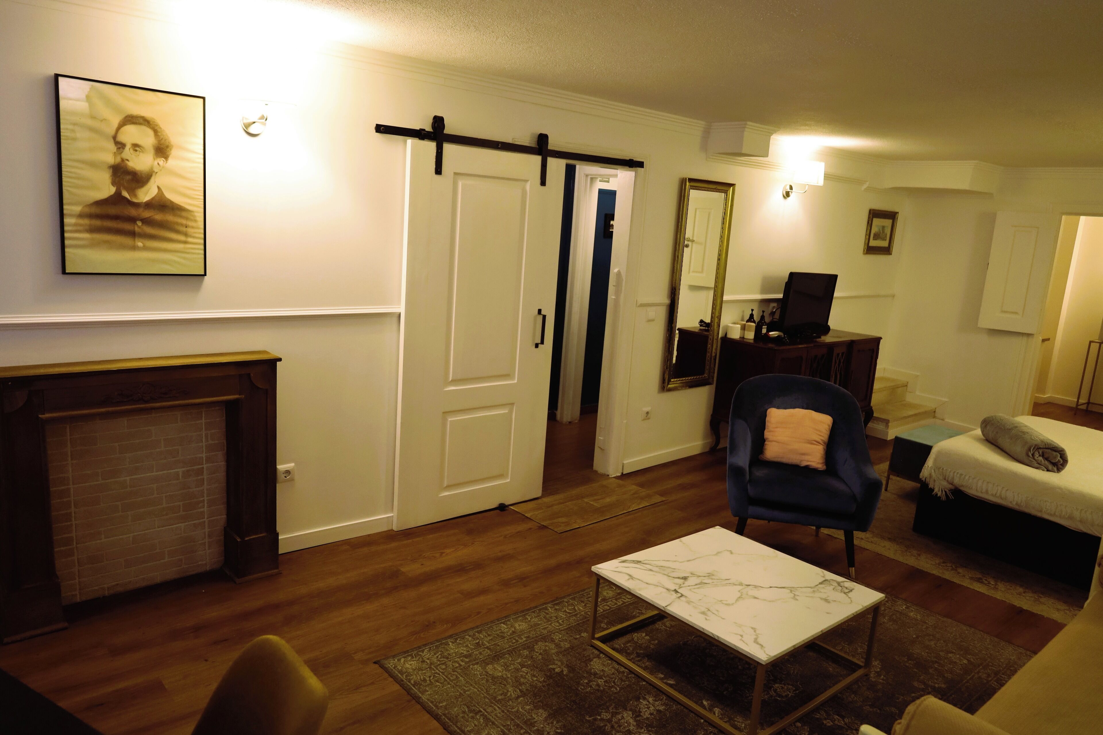 A living room with a fireplace, a sofa, a chair, a bed, and a desk with a computer.