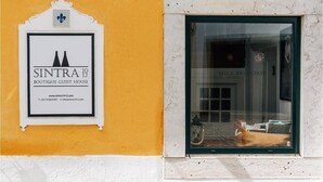 A sign for Sintra Boutique Guest House with contact information and a window displaying a bed and breakfast sign.