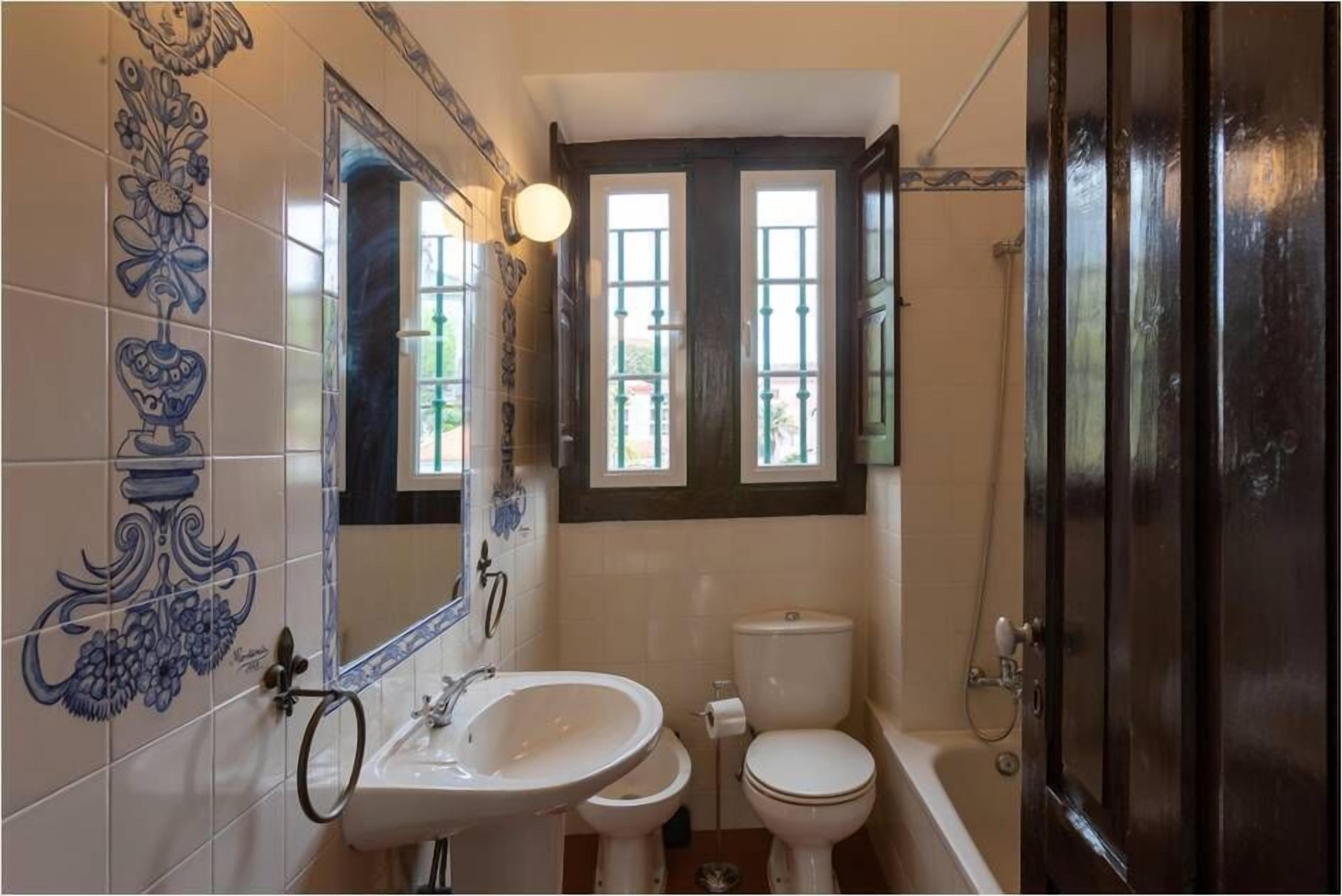 Un bagno con lavandino, WC e vasca da bagno. Le pareti sono rivestite di piastrelle decorative e c'è una finestra sopra il water.