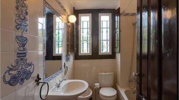 Un bagno con lavandino, WC e vasca da bagno. Le pareti sono rivestite di piastrelle decorative e c'è una finestra sopra il water.