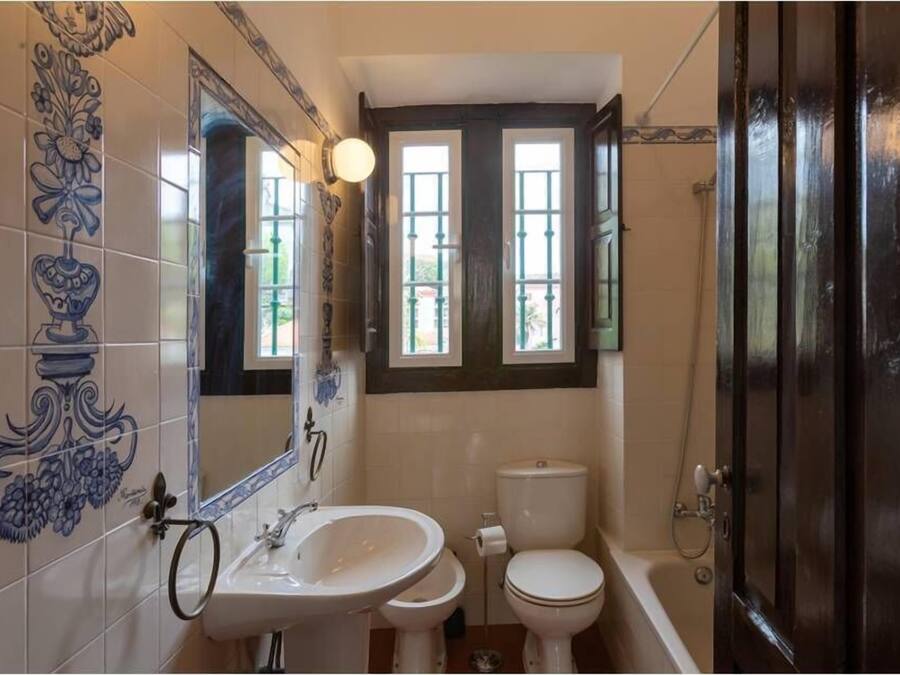 Un bagno con lavandino, WC e vasca da bagno. Le pareti sono rivestite di piastrelle decorative e c'è una finestra sopra il water.