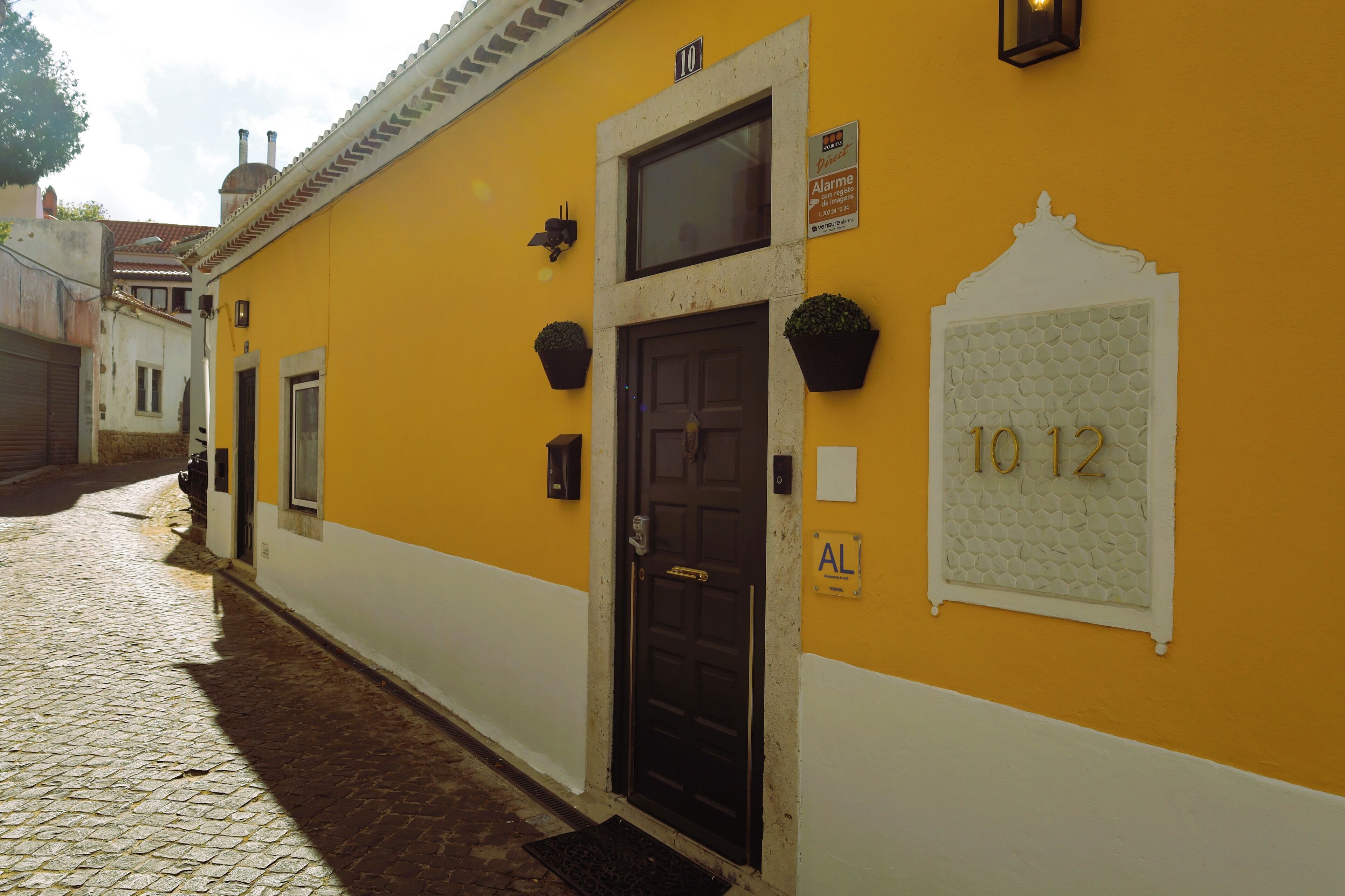 Un bâtiment jaune avec une porte noire, une fenêtre et le numéro « 1012 » inscrit sur le mur.